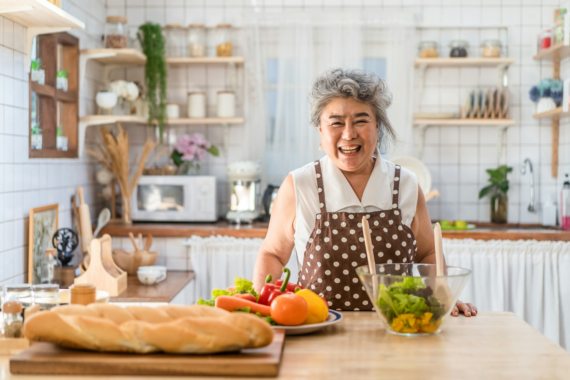 Asian senior elderly grandmother cooking salad dish at counter in kitchen with happiness at home