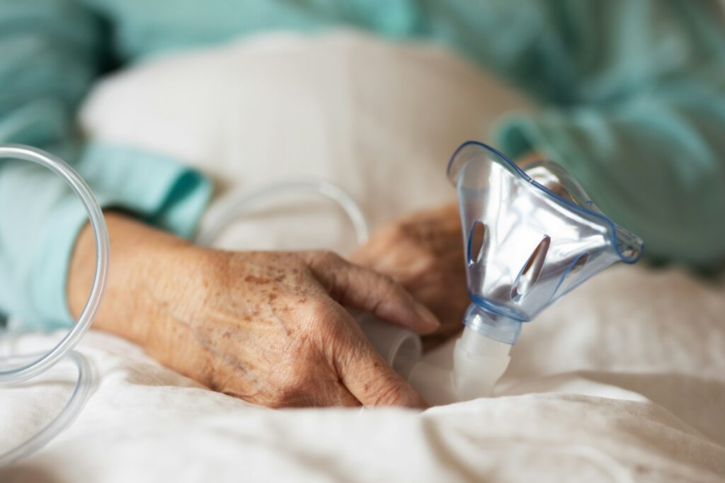 Close-up of oxygen mask holding by eldery patient. Home oxygen therapy.