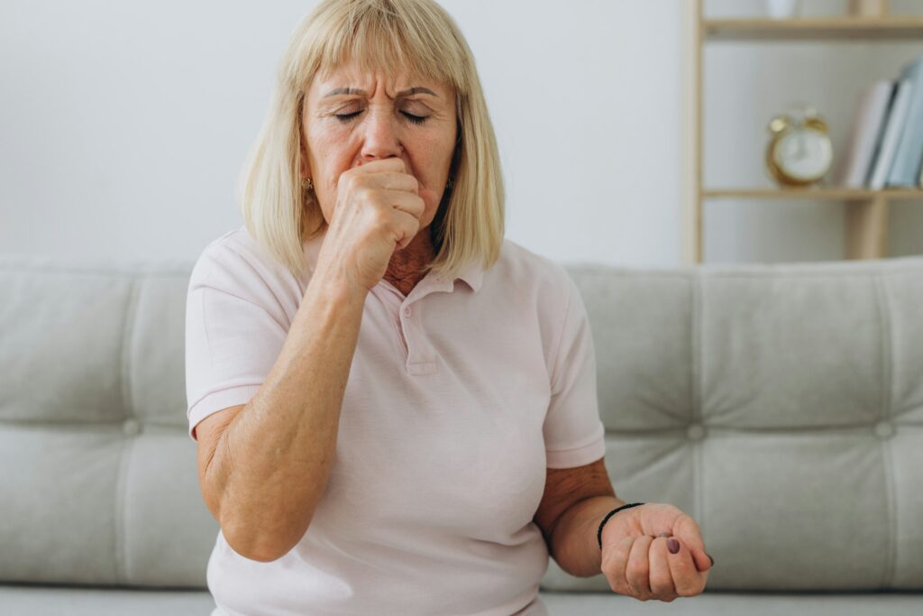Senior woman sitting indoors while coughing