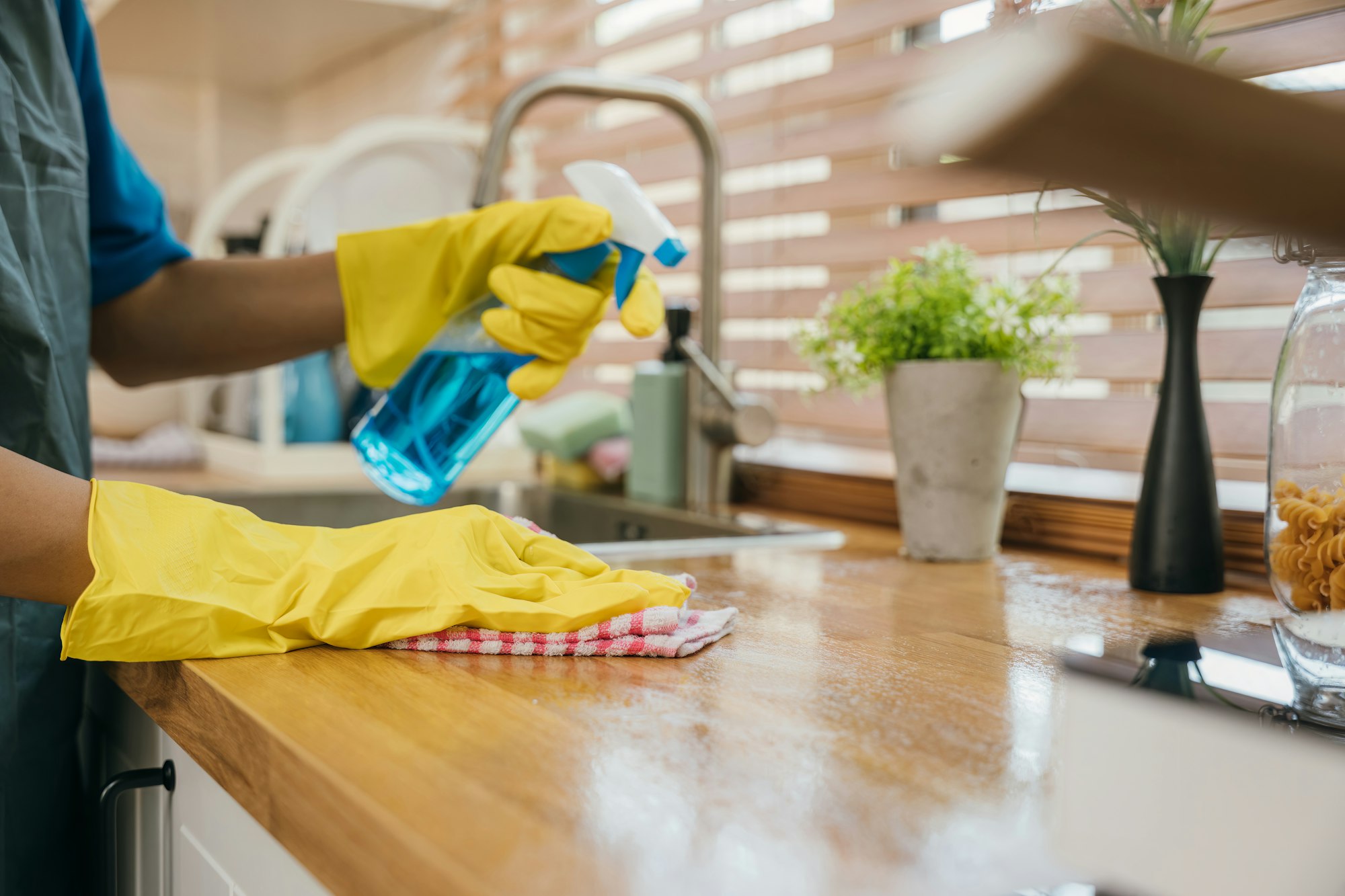 Woman in uniform smiling cleaning kitchen desk with disinfectant spray. Housekeeping hygiene concept